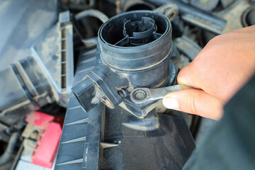 A mechanic's hand tightens a bolt on a car engine using a wrench. The image conveys the process of...