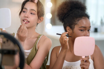 Two girls of different ethnicities and skin tones are live streaming a makeup tutorial for social...