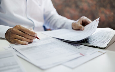 asian businessman holding pen reviewing document and business contract on desk in office using computer laptop working and meeting online