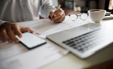 asian businessman checking business contract using mobile phone and laptop working at home office, working at home concept