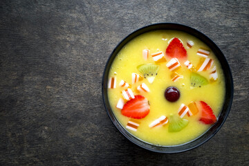 A tropical smoothie bowl with mango, kiwi and strawberry fruits, on an old wooden table