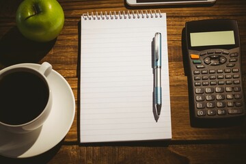 Close-up of coffee cup by book with apple and calculator