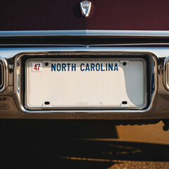 Close-up of a North Carolina license plate on a vintage car, with "Text Space" in blue letters, reflecting warm sunlight