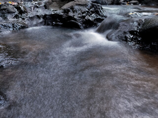 Close-up of a gentle river stream captured in long exposure, flowing between dark rocks.