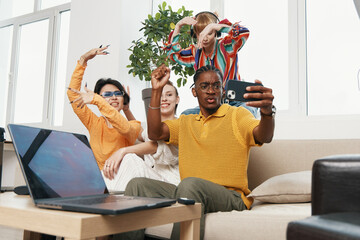 Young adult coworkers socializing and taking selfie together at workplace, diverse business friends...