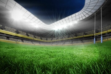 Floodlights lighting empty seats under curved roof as turf covering field with blue-padded posts