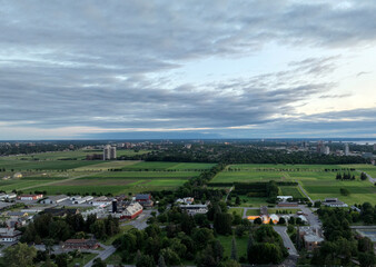 Fototapeta premium The expansive agricultural fields of Ottawa's Central Experimental Farm stretch towards the distant city skyline, bordered by urban development under a cloudy sky