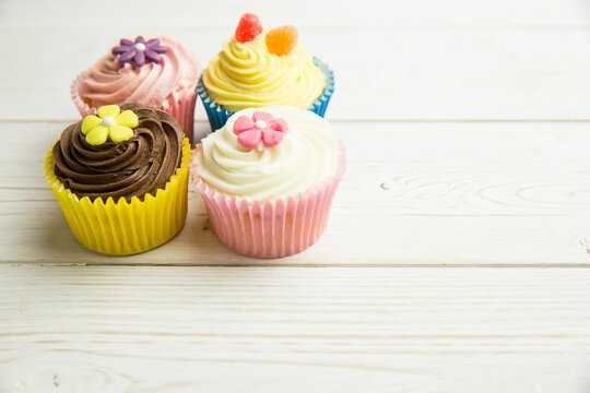 Naklejki Four decorated cupcakes are sitting on pale wood tabletop in flat design with sugar flower toppings