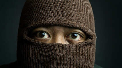 Close-up portrait of man with brown cloth mask covering face except eyes, intense and secretive...