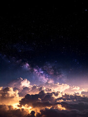 Fototapeta premium A mesmerizing vertical shot reveals a vibrant purple and pink nebula and countless stars in the upper night sky, transitioning to dramatic, illuminated clouds glowing orange and yellow below. This cos