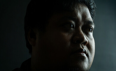 Bearded Indonesian man on black background, neutral expression in low-key lighting, simple portrait...