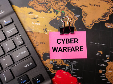 Black keyboard and sticky note with the word CYBER WARFARE on a world map background