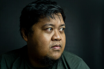 Bearded Indonesian man on black background, neutral expression in low-key lighting, simple portrait...