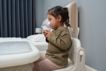 toddler girl making inhalation treatment with nebulizer at home