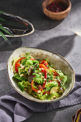 Vegetable salad with lettuce, red pepper and zucchini in moody lighting, overhead ceramic bowl composition