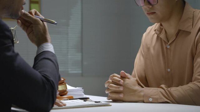Lawyer questioning stressed suspect experiencing intense headache during legal consultation, articulating mounting pressure and mental strain in professional office setting