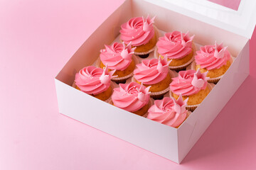 Beautiful cupcakes with pink whipped cream cheese topping. A box of birthday cupcakes on a pink pastel background. Festive dessert delivery concept