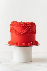Delicate lambeth style birthday cake with red cream cheese frosting decorated with cream tracery and golden sprinkles. White background