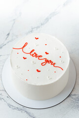 White chocolate cake decorated with red I love you text. Stylish cake for a beloved one. Valentine's cake on the white marble background