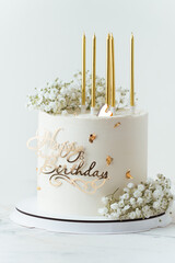 Beautiful white birthday cake decorated with golden candles and field  gypsophila flowers on the white background