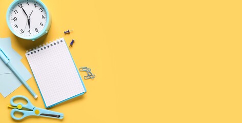 Notebook, alarm clock and stationery on yellow background with space for text