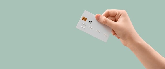 Hand holding credit card on turquoise background with space for text