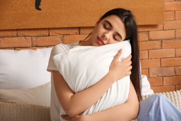 Young woman hugging soft pillow in bedroom