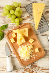 Board with tasty Swiss cheese and grapes on light wooden background
