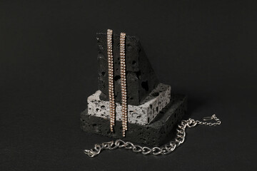 Decorative podium with beautiful chain bracelet and earrings on black background