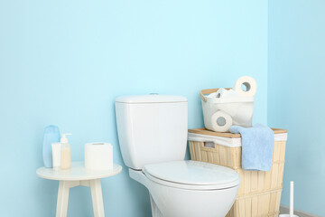 Ceramic toilet bowl, basket with paper rolls and cosmetic products near color wall