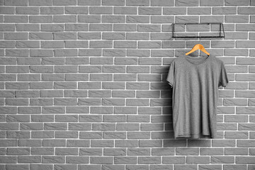 Stylish t-shirt hanging on grey brick wall