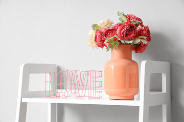 Vase with bouquet of beautiful artificial flowers on shelving unit near white wall, closeup
