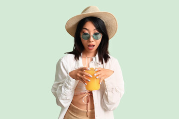 Surprised Asian woman with jug of juice on green background