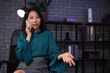 Happy Asian businesswoman talking by mobile phone and working in office