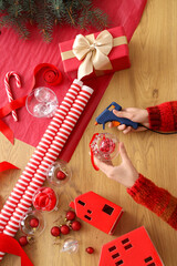 Woman holding glue gun and decorating Christmas ball with rhinestones on table