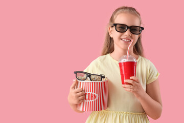 Happy little girl in 3D cinema glasses with popcorn bucket and cup of cola on pink background