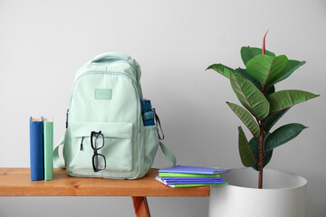 School backpack, stationery, eyeglasses and houseplant on wooden table near light wall