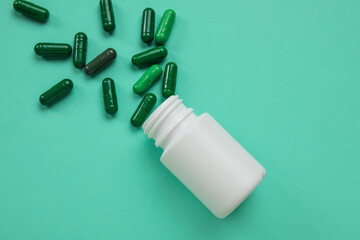 Jar with scattered pills on turquoise background