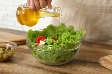 Woman adding olive oil into bowl with tasty salad at table in kitchen