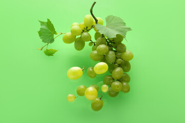 Flying sweet green grapes with leaves on color background