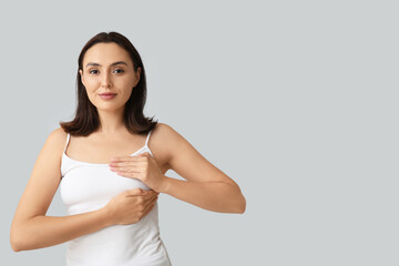 Young woman checking her breast on light background. Cancer awareness concept