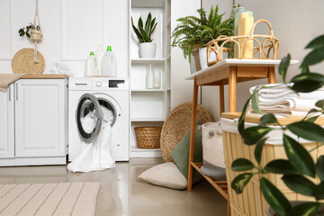 Interior of stylish laundry room with washing machine, houseplants and cleaning supplies