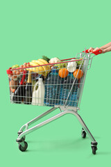 Woman pushing shopping cart full of different food on green background
