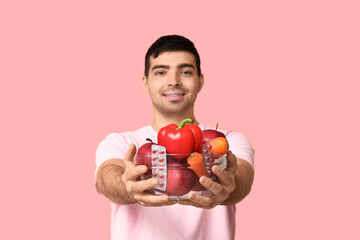 Young man with vitamin A pills and healthy food on pink background