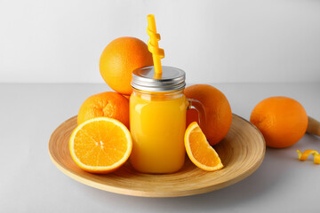 Mason jar of fresh orange juice and plate with fruits on white background