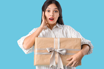 Beautiful shocked Asian woman with gift box on blue background