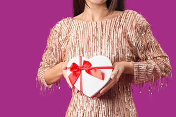 Beautiful young Asian woman with gift box for Valentine's Day on purple background, closeup