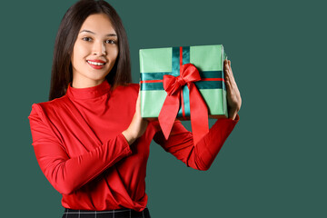 Beautiful young Asian woman with gift box on green background