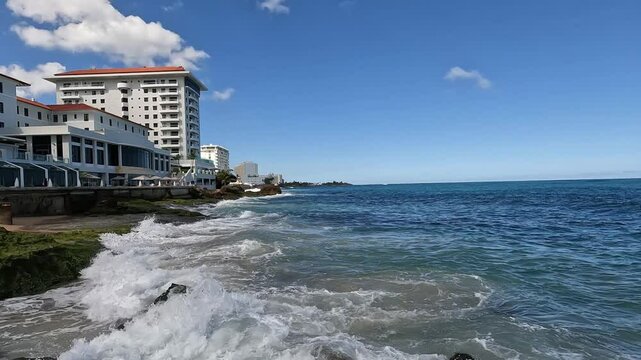 waves crashing on the shore of old san juan puerto rico with tall hotel building in the background (caribbean travel tourism destination) sj pr sea coast rocky shore beach condado