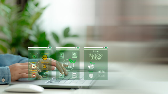 Hands typing on laptop with net zero carbon hologram dashboards showing CO2 alerts, eco data, and sustainability icons, representing digital environmental monitoring and green technology.